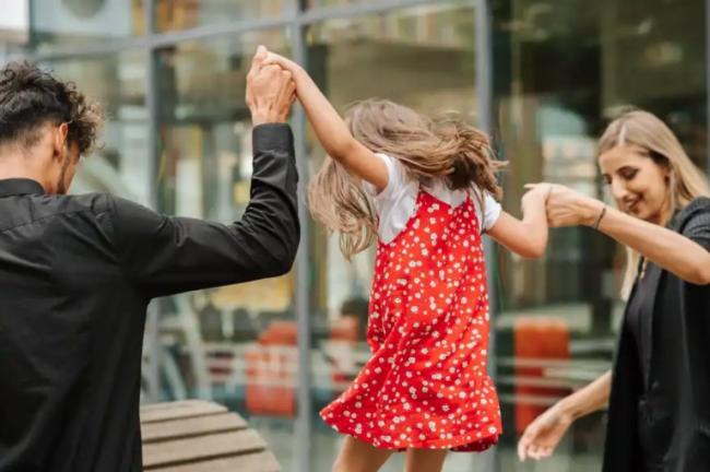 Two parents holding their daughter as she walks on a high bench.